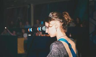 young female caucasian singer performing a song on a stage. singing woman, emotional passionate vocalist. rock music public concert. rear view photo