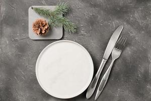 empty plate with silverware and christmas tree branch and cone on grey table. copy space. table setting template for new year or christmas menu. restaurant menu mock up. top view photo