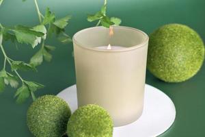 green scented candle with herbal fragrance for cozy home atmosphere. burning flame, winter house comfort and cosiness. hygge concept photo