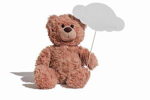 teddy bear sitting on a white background and holding a message cloud on a stick. copy space for text. kids mockup bubble ot template for inscription. photo