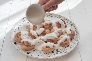 human hand pouring milk sauce on cinnamon swirls. photo