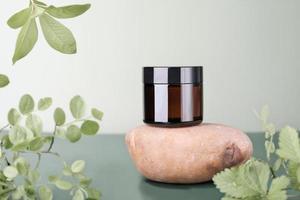 unbranded brown glass jar on natiral stone podium and green branches and leaves. cosmetic product, collagen peptides face and body care, anti age therapy. photo