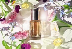 a bottle of perfume oil with summer flowers and green leaves. flat lay. top view. summer perfume and fragrances photo
