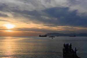 sunset on a sea. unrecognizable fishermen catching fish photo