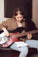 young woman playing bass guitar and looking at chords notes. rehearsal room. female rock musician. vertical size photo
