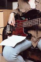 Vista recortada de una mujer joven que toca la guitarra eléctrica. bajista leyendo notas de acordes y tocando en el estudio foto