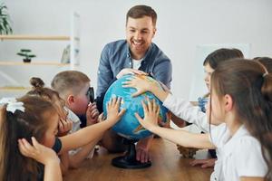 Learning geography by using Earth globe. Group of children students in class at school with teacher photo