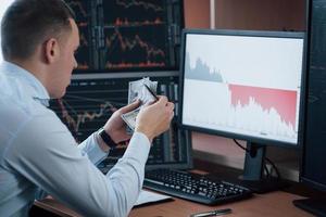 Enough money for today. Man working online in the office with multiple computer screens in index charts photo