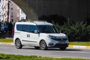 antalya, turquía, 04 de marzo de 2022, el fiat doblo blanco conduce rápido por la calle en un cálido día de verano con el telón de fondo de un puente foto