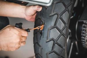 Rider use a tire plug kit and trying to fix a hole in tire's sidewall ,Repair a motorcycle flat tire in the garage. motorcycle maintenance and repair concept photo