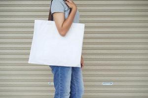 mujer hipster sosteniendo una bolsa de mano blanca para una plantilla en blanco simulada foto