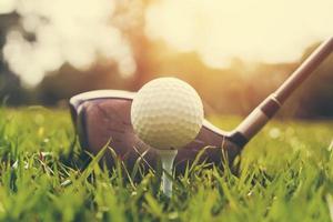 club de golf de primer plano y pelota de golf sobre hierba verde con puesta de sol foto