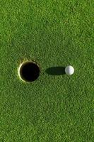 golf ball on green grass with hole and sunlight photo