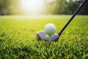 closeup golf club and golf ball on green grass wiht sunset photo