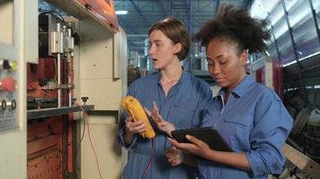 Two professional female engineer workers in safety uniforms work by inspecting machines' voltage current, checking, and maintaining at manufacturing factory, electric system service occupations. video