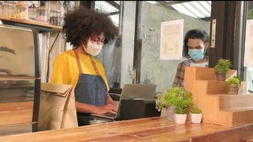 barista afro-americana com máscara facial trabalha no café com distanciamento social, café para viagem para um cliente, novo serviço normal de cafeteria para pequenas empresas no estilo de vida de quarentena covid19. video