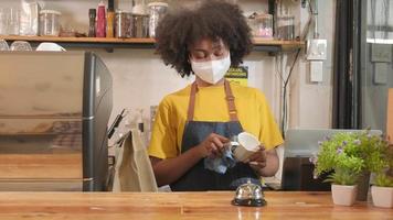 la barista afroamericana trabaja limpiando la taza de café, mirando a través de la ventana del café, esperando a los clientes en un nuevo servicio de estilo de vida normal, el impacto comercial de la cuarentena pandémica covid-19.