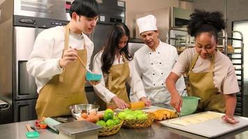 curso de culinária, um chef masculino sênior em uniforme de cozinheiro ensina jovens alunos de aulas de culinária a preparar ingredientes e massa de pastelaria para alimentos de padaria e tortas de frutas em uma cozinha de aço inoxidável de restaurante.