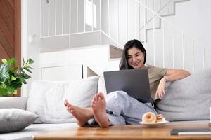 mujer joven asiática mirando una computadora portátil riéndose con buenas noticias o cupón de descuento para comprar en línea en casa. mujer feliz y alegre mirando en la computadora portátil leer el mensaje sentirse emocionada foto