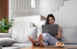 Young business freelance Asian woman working on laptop checking social media while lying on the sofa when relax in living room at home. photo