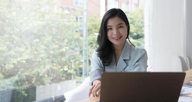 Charming Asian woman working at the office using a laptop Looking at the camera. photo