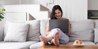 mujer joven asiática mirando una computadora portátil riéndose con buenas noticias o cupón de descuento para comprar en línea en casa. mujer feliz y alegre mirando en la computadora portátil leer el mensaje sentirse emocionada foto