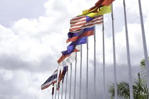 muchas de las banderas de la asean en los coloridos colores soplados por la fuerza del viento ondeando en un poste frente a un hotel en tailandia sobre un fondo con nubes y cielos azules. foto