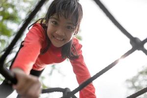 linda niña pequeña divirtiéndose en el patio de recreo, trepando y deslizándose hacia abajo foto