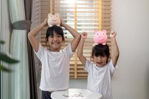 Little Asian girl saving money in a piggy bank, learning about saving, Kid save money for future education. Money, finances, insurance, and people concept photo