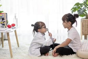 dos lindos niños juegan al médico y al hospital usando estetoscopio. amigas chicas divirtiéndose en casa o en preescolar. foto