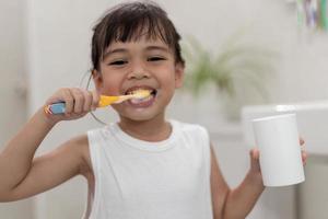 pequeña y linda niña limpiándose los dientes con un cepillo de dientes en el baño foto