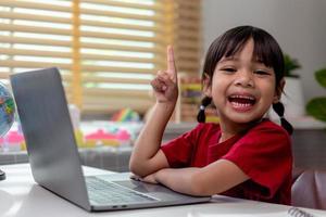 niña asiática que usa una computadora portátil para estudiar en línea la educación en el hogar durante la cuarentena en el hogar. educación en el hogar, estudio en línea, cuarentena en el hogar, aprendizaje en línea, virus corona o concepto de tecnología educativa foto