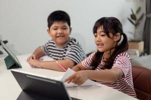 Asian boys and girls enjoy online learning by taking notes and using tablets at home. photo