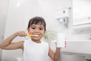 pequeña y linda niña limpiándose los dientes con un cepillo de dientes en el baño foto