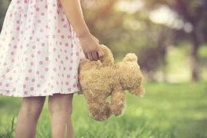 Rear view of little girl looking her future.Close up of hands of a female child holding a teddy bear. Girl standing holding a brown furry teddy bear.Vintage color photo