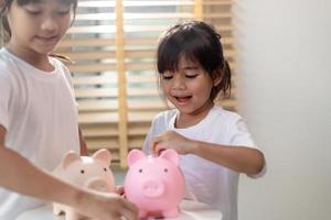 niña asiática ahorrando dinero en una alcancía, aprendiendo a ahorrar, los niños ahorran dinero para la educación futura. concepto de dinero, finanzas, seguros y personas foto