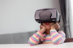 niño con casco de realidad virtual sentado detrás de la mesa en casa foto
