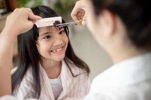 Asian Mother cutting hair to her daughter in living room at home while stay at home safe from Covid-19 Coronavirus during lockdown. Self-quarantine and social distancing concept. photo