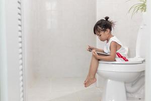 niño sentado en el inodoro sosteniendo la tableta.concepto de teléfono inteligente adicto al niño foto
