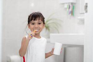 pequeña y linda niña limpiándose los dientes con un cepillo de dientes en el baño foto