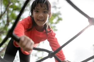 linda niña pequeña divirtiéndose en el patio de recreo, trepando y deslizándose hacia abajo foto