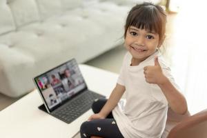 niña asiática tomando clases en línea y feliz por el concepto de pandemia de coranavirus en cuarentena en la escuela en casa foto