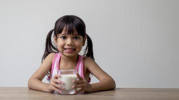 la niña asiática está bebiendo leche de un vaso, estaba muy feliz. foto