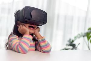 niño con casco de realidad virtual sentado detrás de la mesa en casa foto