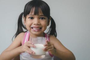 la niña asiática está bebiendo leche de un vaso, estaba muy feliz. foto