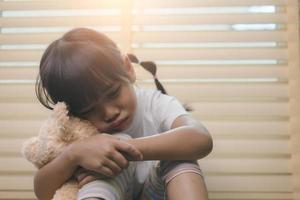 Close up lonely little girl hugging toy, sitting at home alone, upset unhappy child waiting for parents, thinking about problems, bad relationship in family, psychological trauma photo