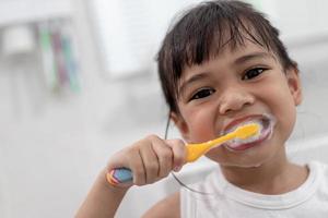 pequeña y linda niña limpiándose los dientes con un cepillo de dientes en el baño foto