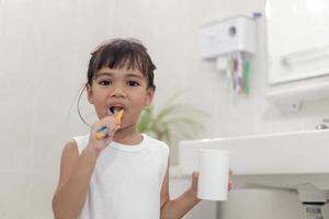 pequeña y linda niña limpiándose los dientes con un cepillo de dientes en el baño foto