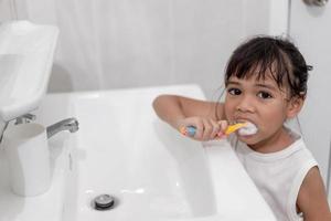 pequeña y linda niña limpiándose los dientes con un cepillo de dientes en el baño foto