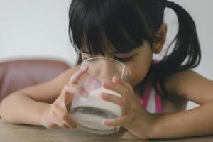 la niña asiática está bebiendo leche de un vaso, estaba muy feliz. foto